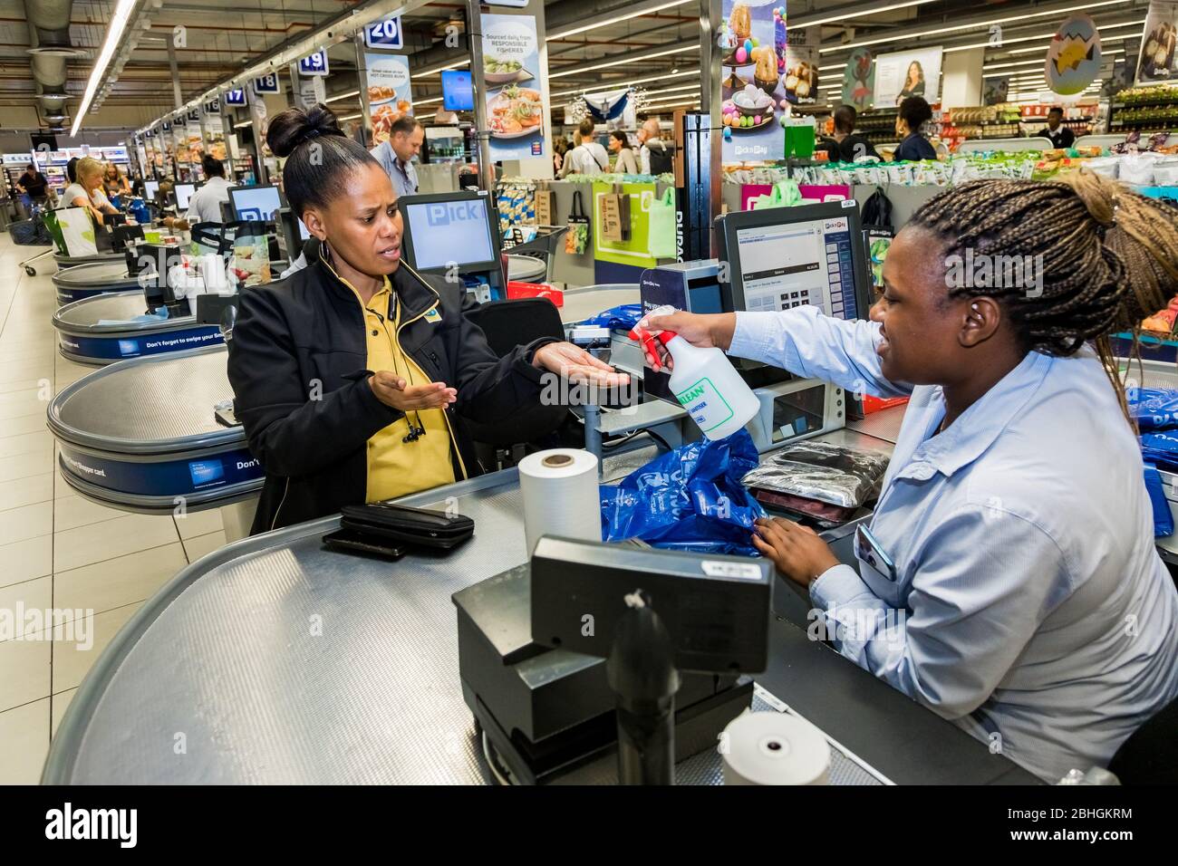 Cape Town, South Africa - March 23, 2020: Checkout cashier staff spraying customer hands with disinfectant at Pick 'n Pay grocery store during virus o Stock Photo