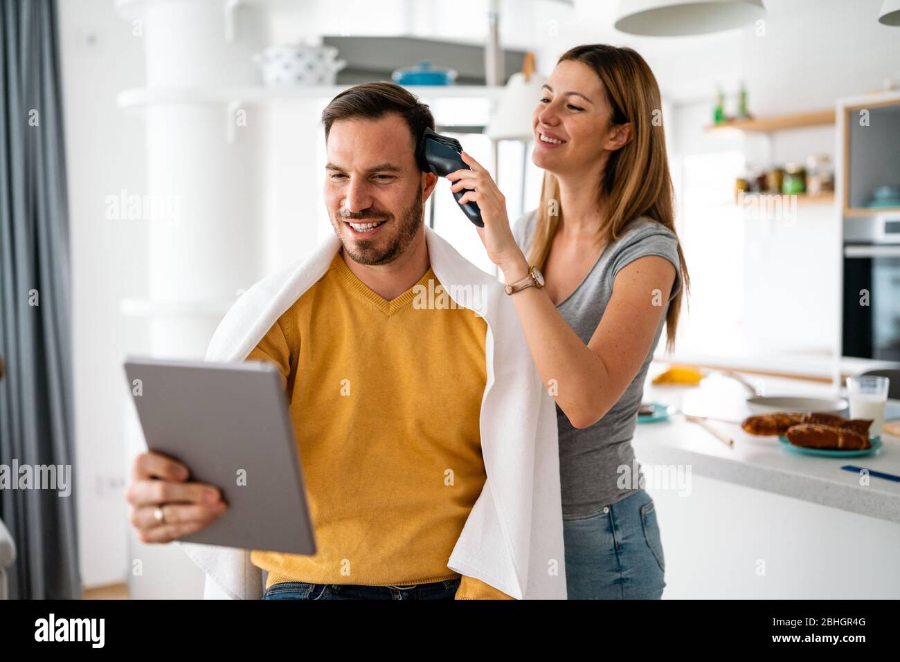 Couple having hair cut at home during quarantine coronavirus pandemic, online hairdressing on tablet Stock Photo