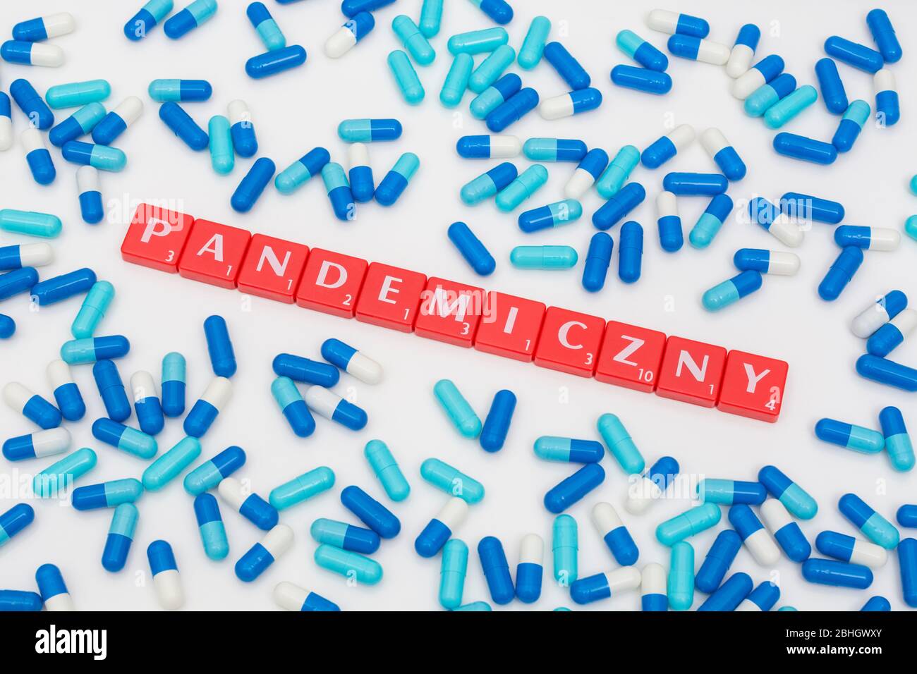 Scattered blue pills caplets and red letter tiles: PANDEMICZNY - Polish adjectival form of word Pandemic. Coronavirus conceptual, Covid 19 metaphor Stock Photo