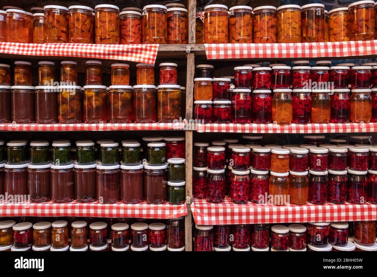 Glass jars with various types of natural delicious jam stand in a row on wooden shelves Stock Photo