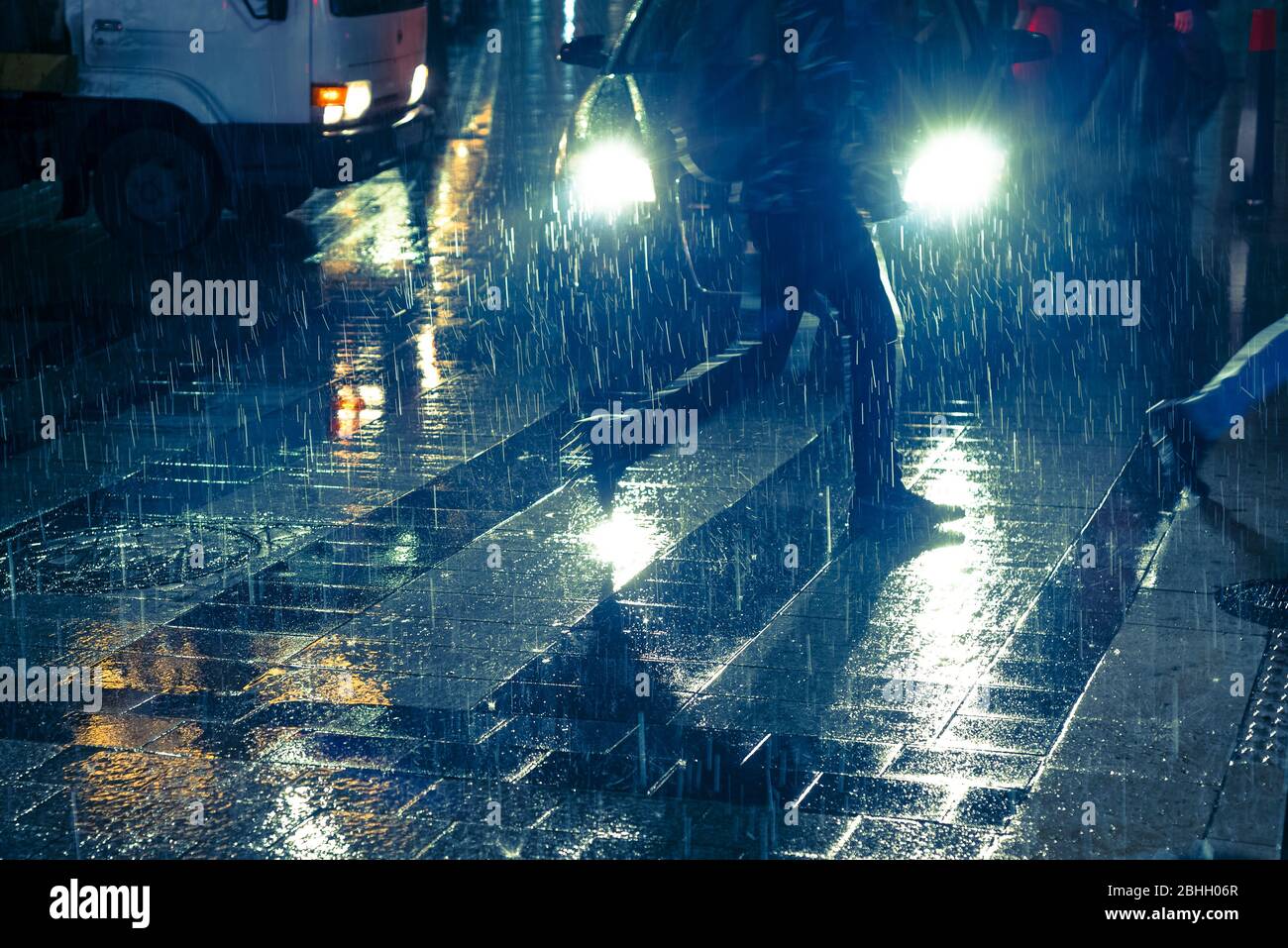 Legs of running people crossing the road against car headlight in the rain Stock Photo