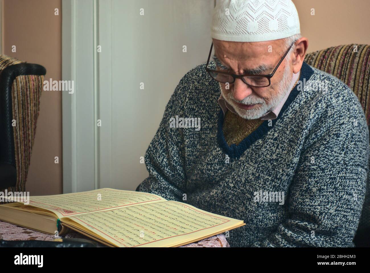 Ankara/Turkey - 24.04.2020: Very old Turkish muslim man wearing a prayer cap reciting the holiest book, Qur'an in Ramadan month Stock Photo