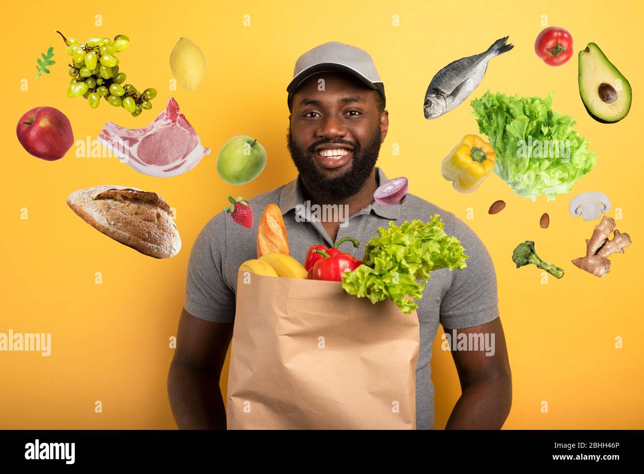 Deliveryman with happy expression ready to deliver bag with food. Yellow background. Stock Photo