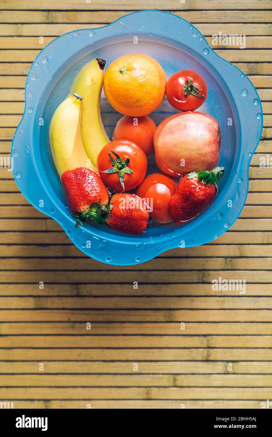 Blue bowl with different fresh and clean fruits on a wooden base. Bananas, tomatoes, apples, strawberries and oranges. Stock Photo