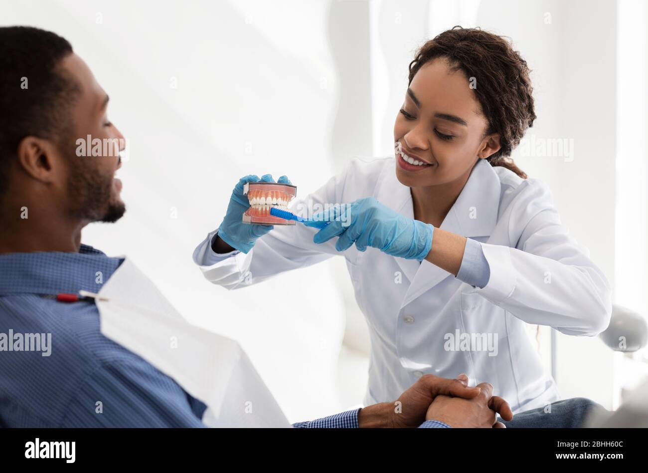 Positive dentist doctor explaining patient how to brush teeth Stock