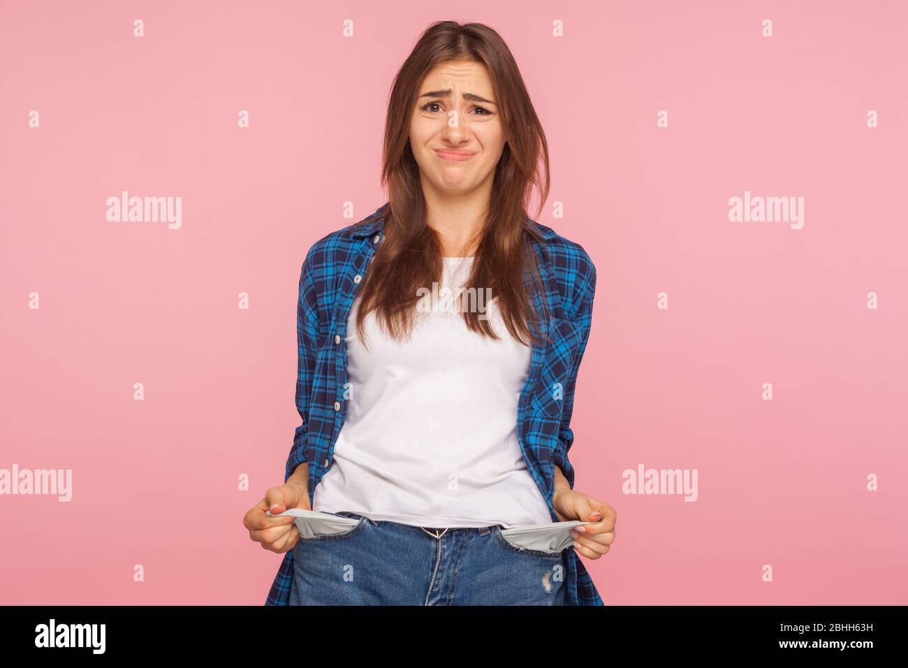 Poor student, unemployment. Portrait of upset jobless girl in checkered shirt turning out empty pockets, showing no money gesture, worried about debts Stock Photo