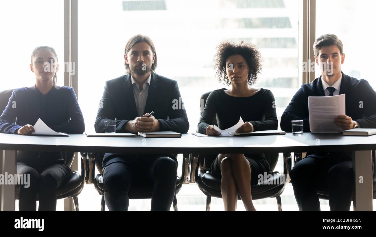 Four confident diverse hr managers sitting at table in row Stock Photo