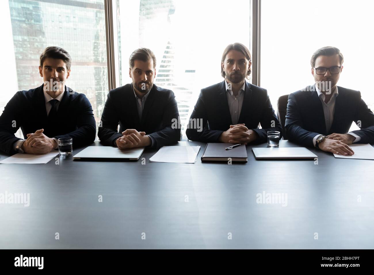 Four serious confident businessmen sitting at table in boardroom Stock Photo