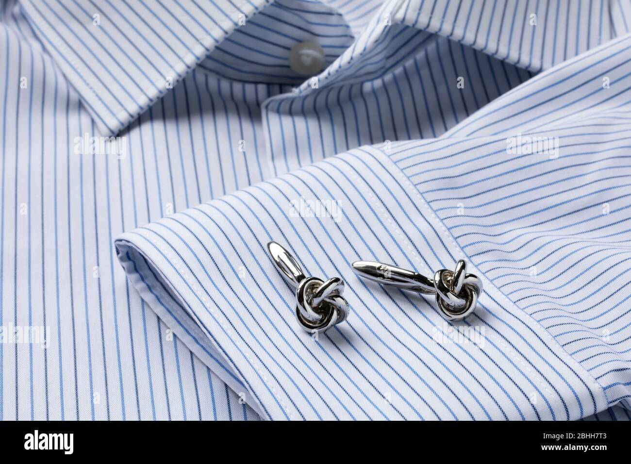 Striped white and blue men's shirt close up with knot shape cufflinks. Close-up. Selecrive focus. Stock Photo