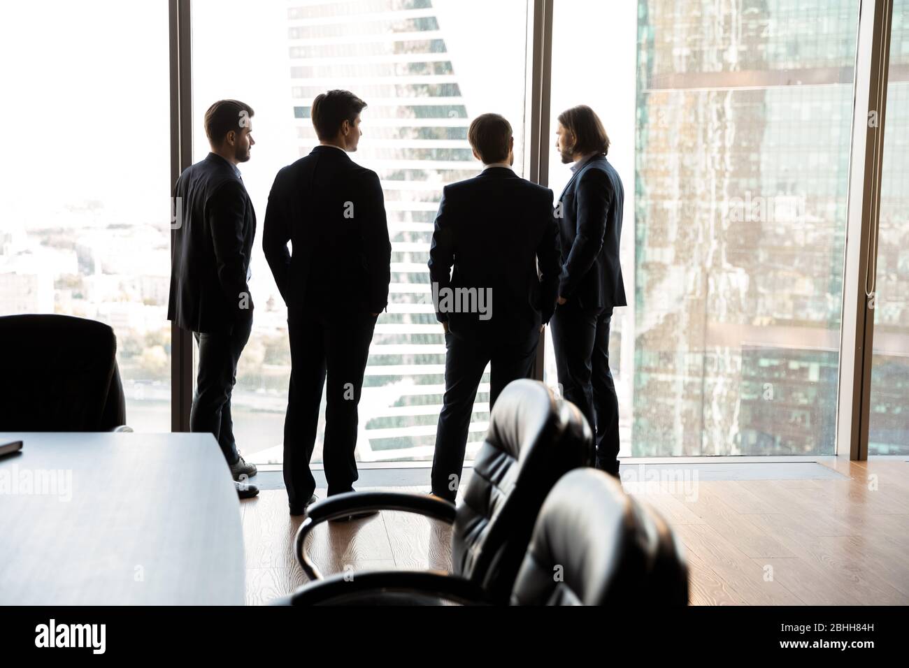 Rear view four confident businessmen looking through panoramic window Stock Photo