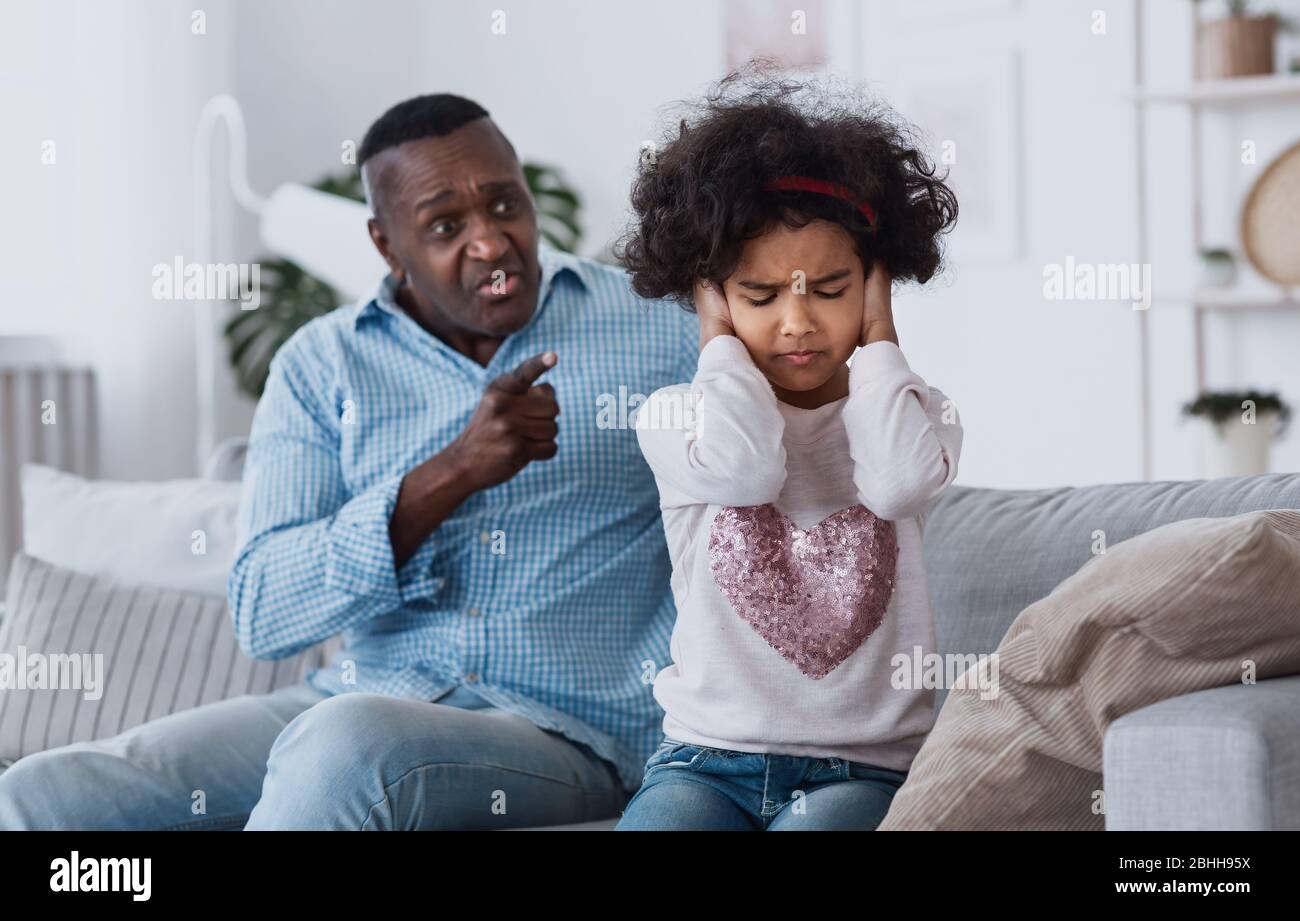 Family conflict caused by coronavirus isolation. Angry granddad and his granddaughter closing her ears indoors Stock Photo