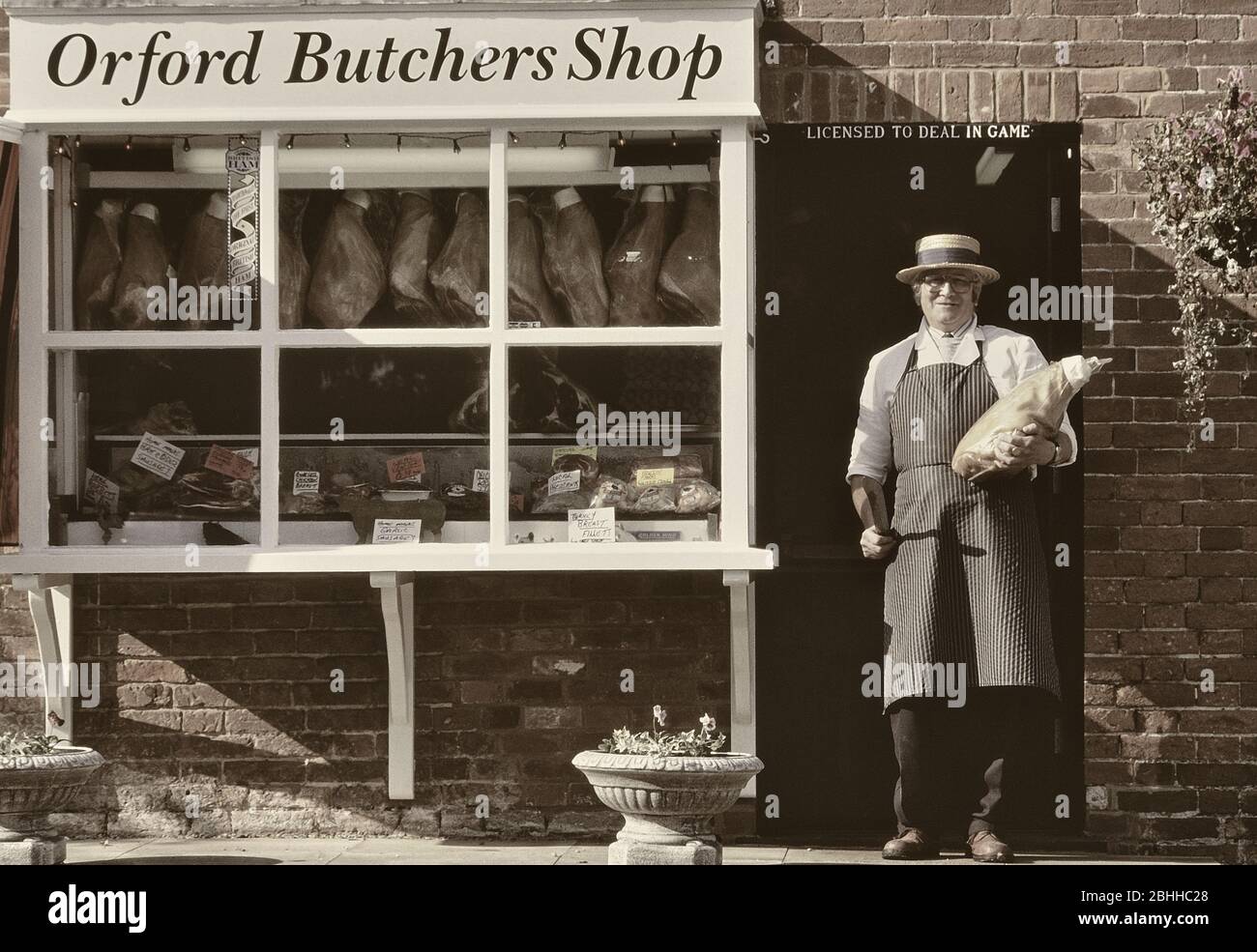 A traditional butcher proudly displays a cut of meat in the doorway of his local butchers shop. Orford. Woodbridge. Suffolk. England. UK Stock Photo