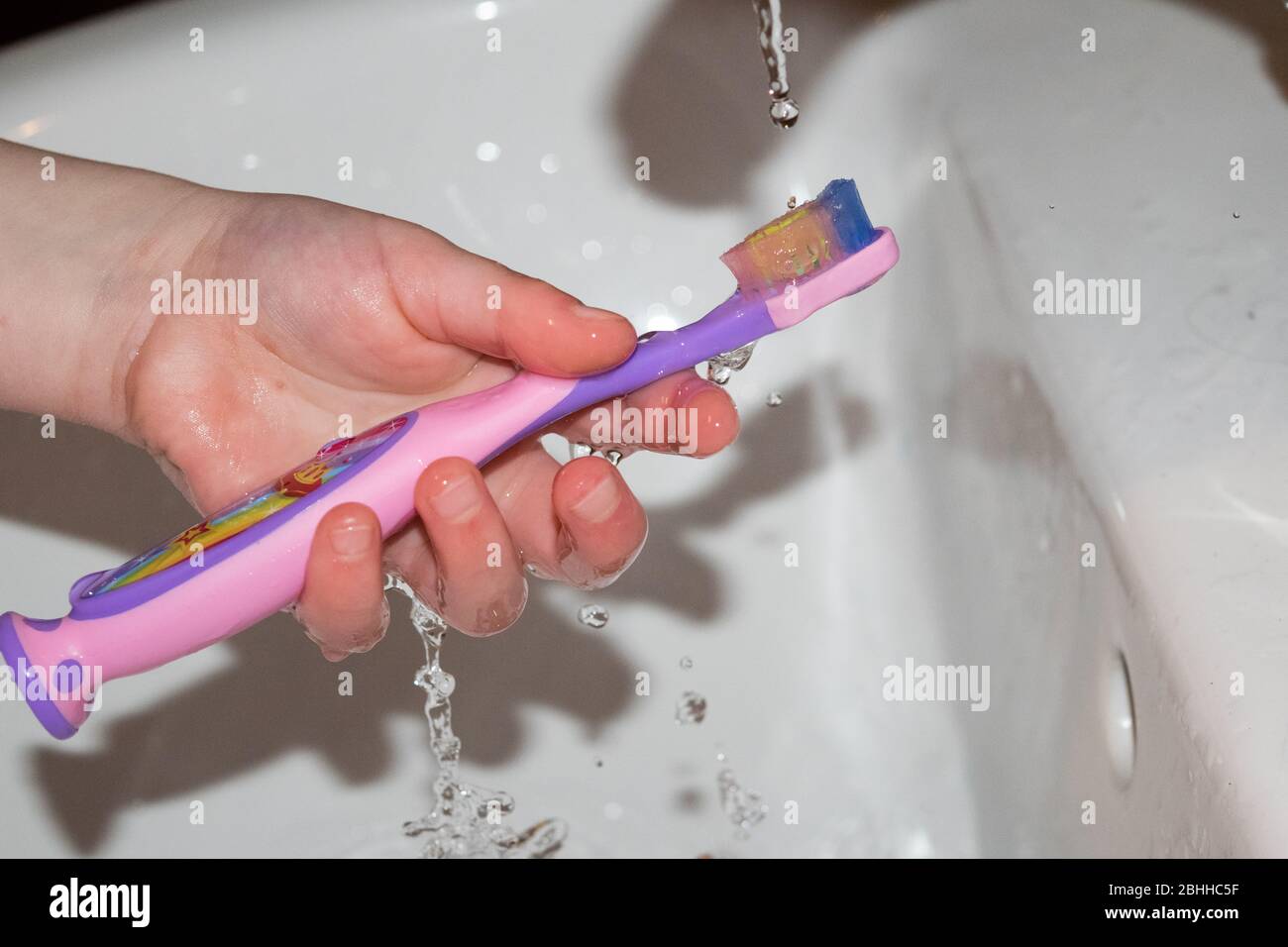 Child holding toothbrush under tap Stock Photo