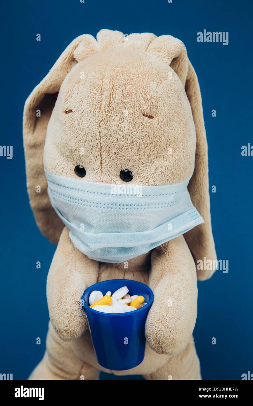 The toy bunny wears a protective medical mask. Flapper holds a glass of pills. Stop coronavirus. Medicine concept Stock Photo