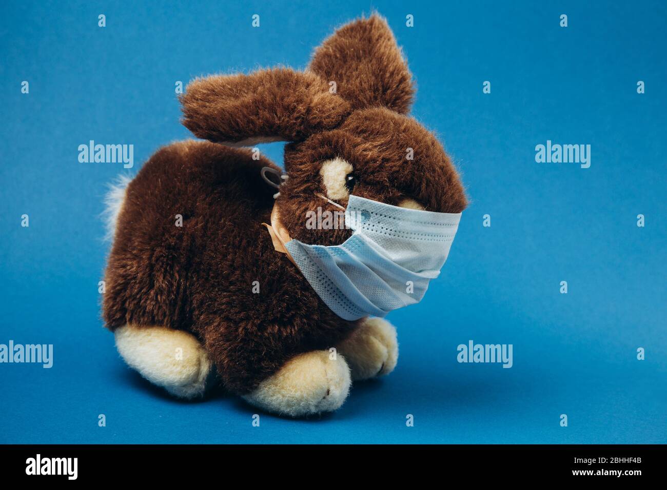 Toy bunny stands in a medical mask on a blue background. Concept of protection from respiratory disease, virus. Stop coronavirus.  Stock Photo