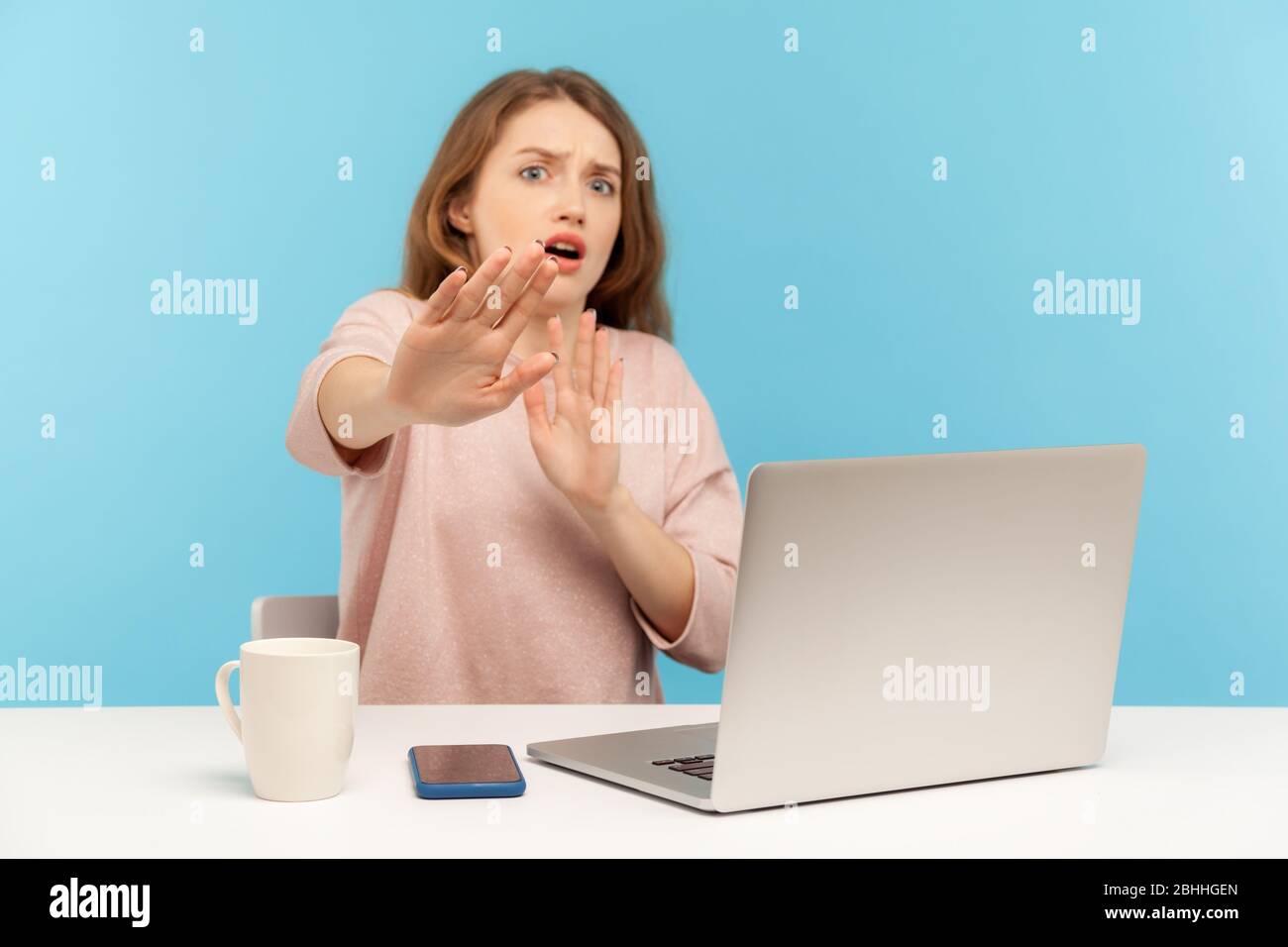No, I'm scared! Frightened woman with shocked expression raising hands in stop gesture, defending herself, freaked out of troubles while working on la Stock Photo