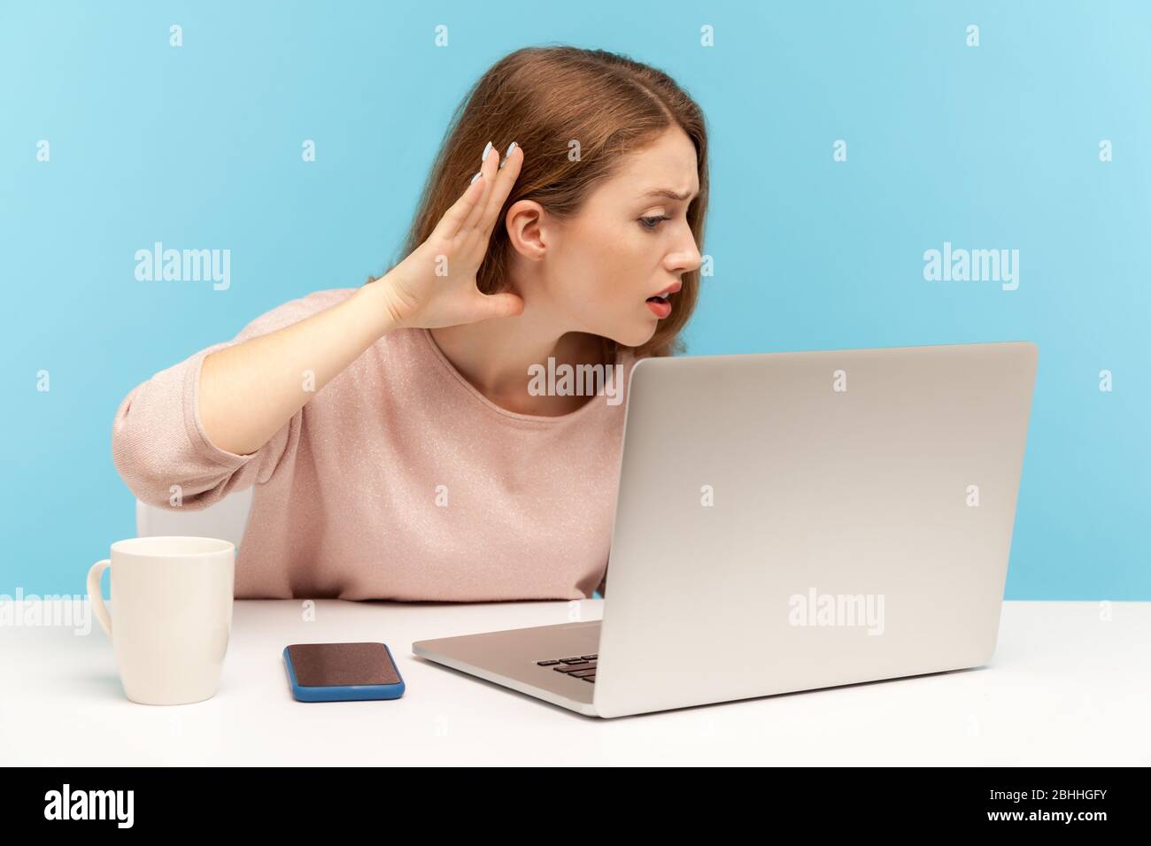 I can't hear, Woman holding arm near ear trying to listen secret talk on video call on laptop, bad internet connection, online conference from home of Stock Photo