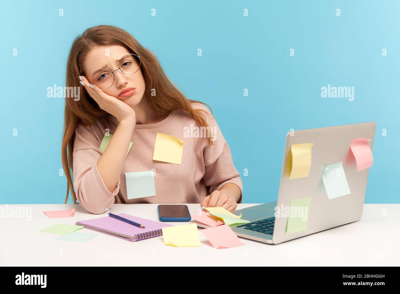 Exhausted overworked woman in nerd glasses sitting covered with sticky notes, looking with bored sleepy expression, tired of workload at home office. Stock Photo