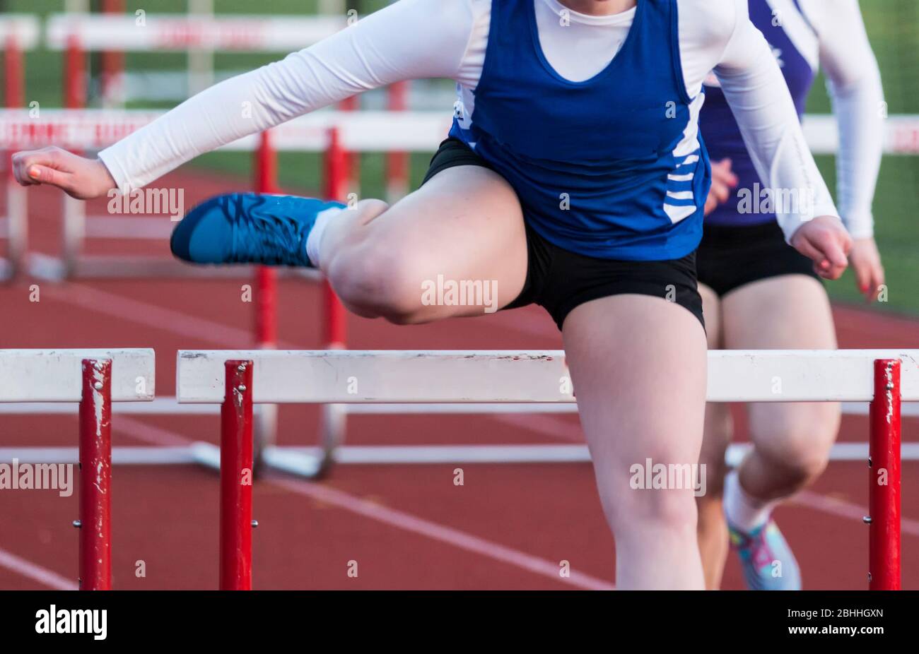 A front view of a high school girl racing the high hurdles in