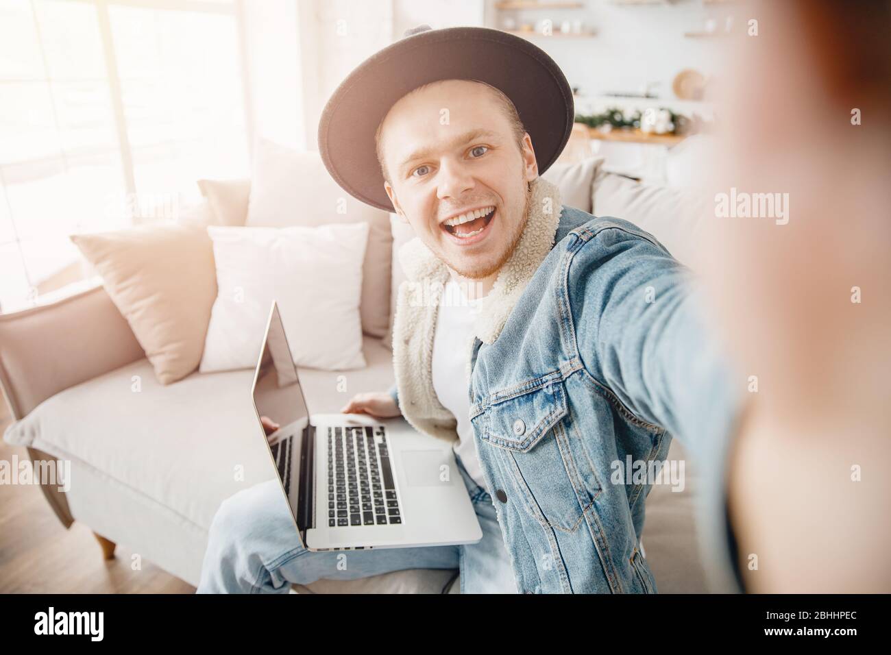 Happy hipster man smile freelancer traveler taking selfie photo in hat, working on laptop home. Concept travel ticket booking Stock Photo