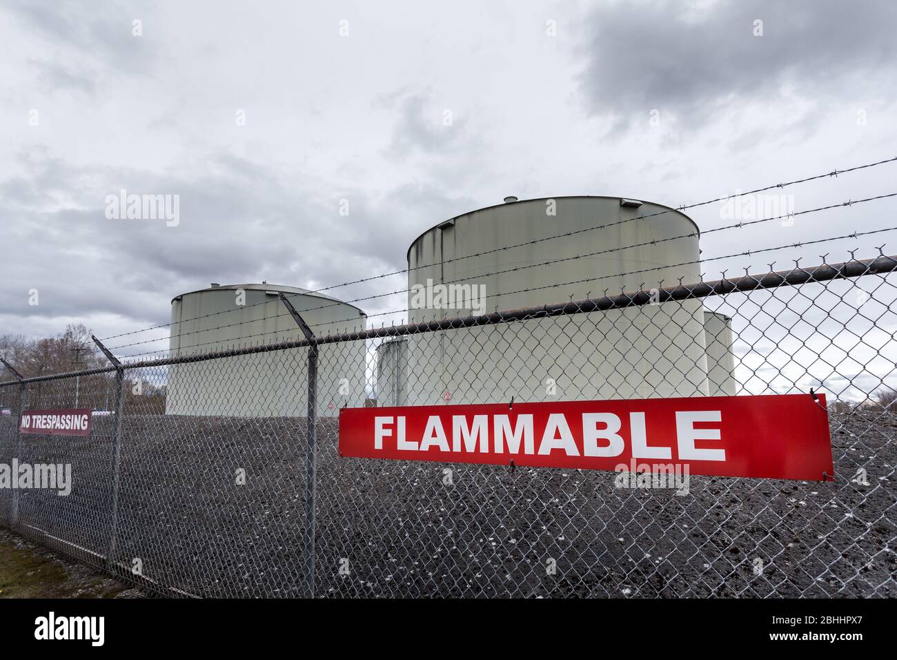 Large jet fuel or oil storage tanks behind a chain link fence with warning signs. Stock Photo