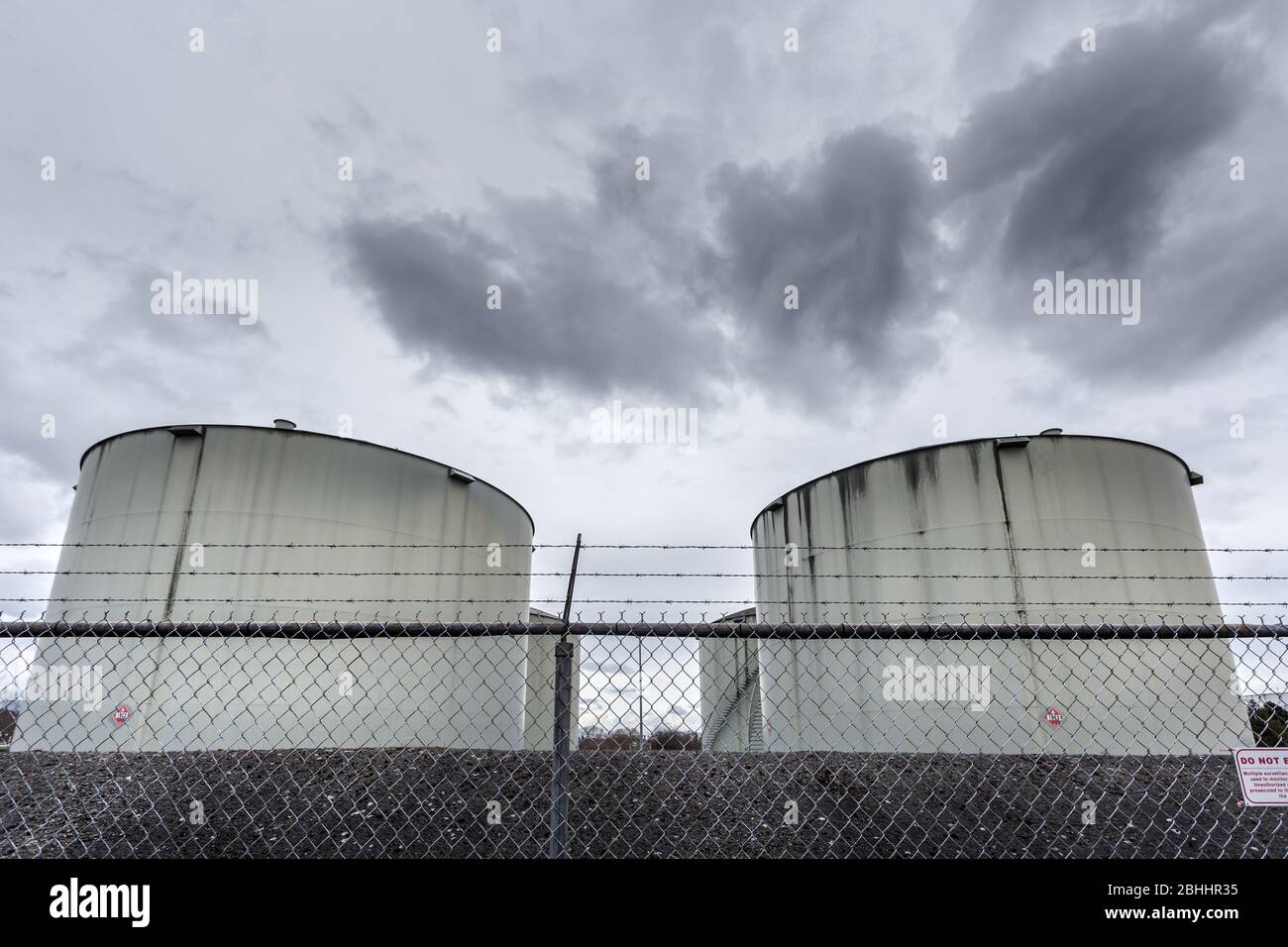 Large jet fuel or oil storage tanks behind a chain link fence with warning signs Stock Photo Alamy