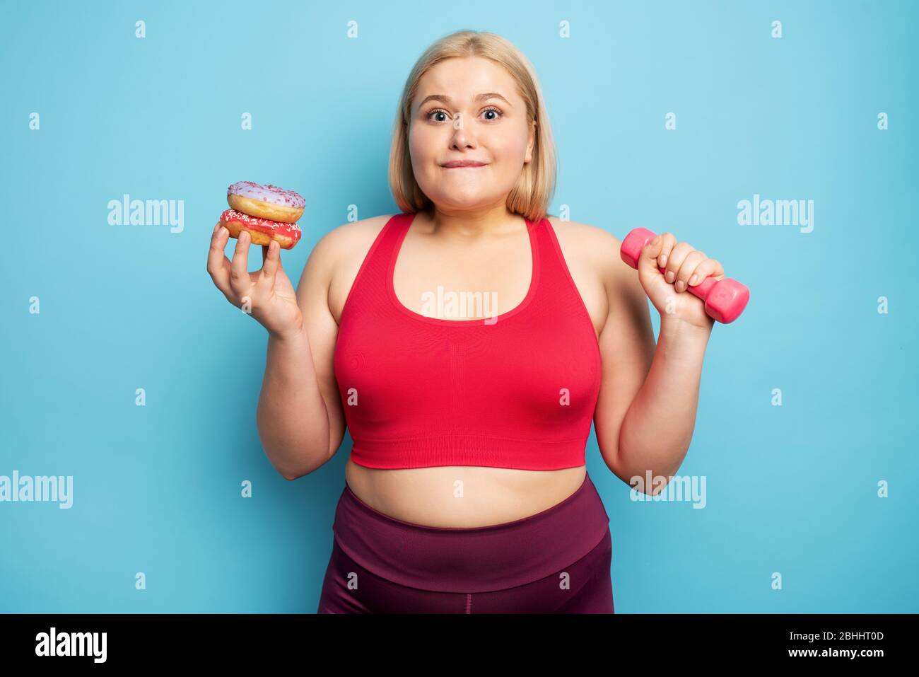 Fat girl thinks to eat donuts instead of does gym. Concept of indecision and doubt Stock Photo
