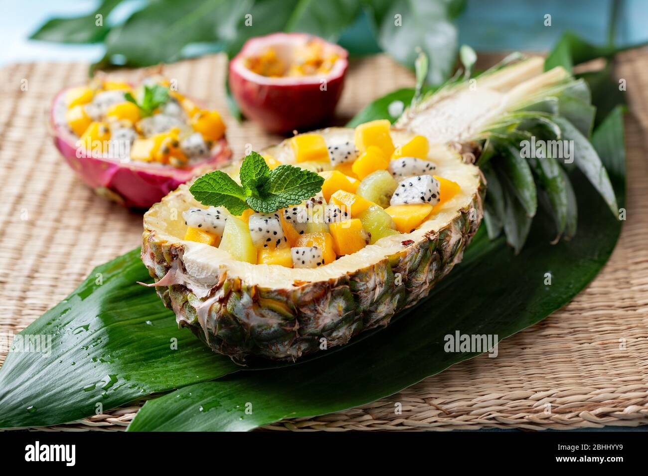 tropical fruit salad in a pineapple half on a straw background Stock Photo