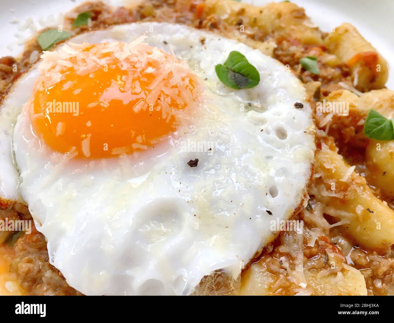 Over easy fried egg with cheese sprinkled on top of Italian food Stock Photo