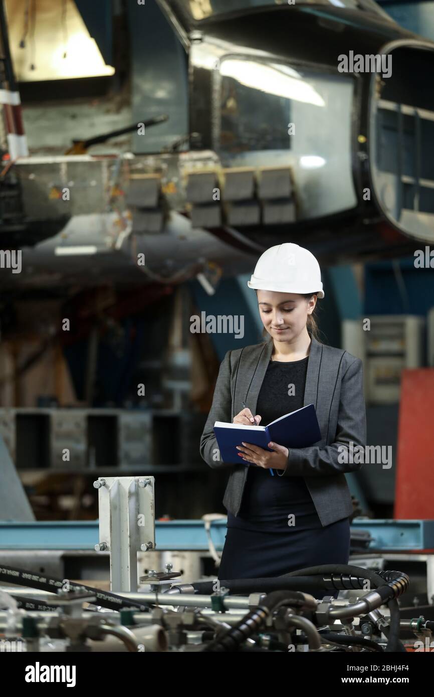Portrait of a female factory manager in a white hard hat and business suit. Controlling the work process at the airplane manufacturer. Stock Photo