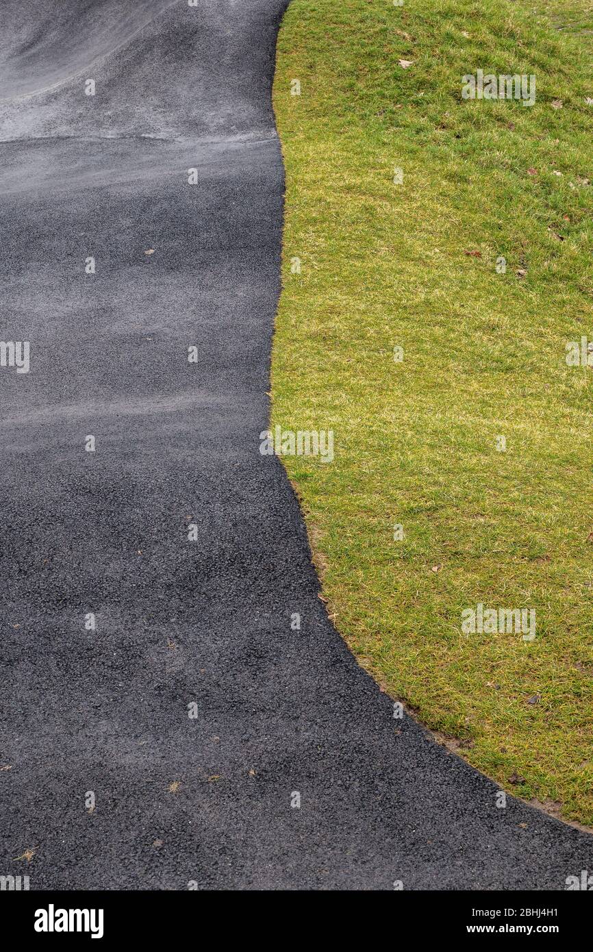 Two halves contrasting background of grass lawn and black asphalt of a bicycle pump track Stock Photo