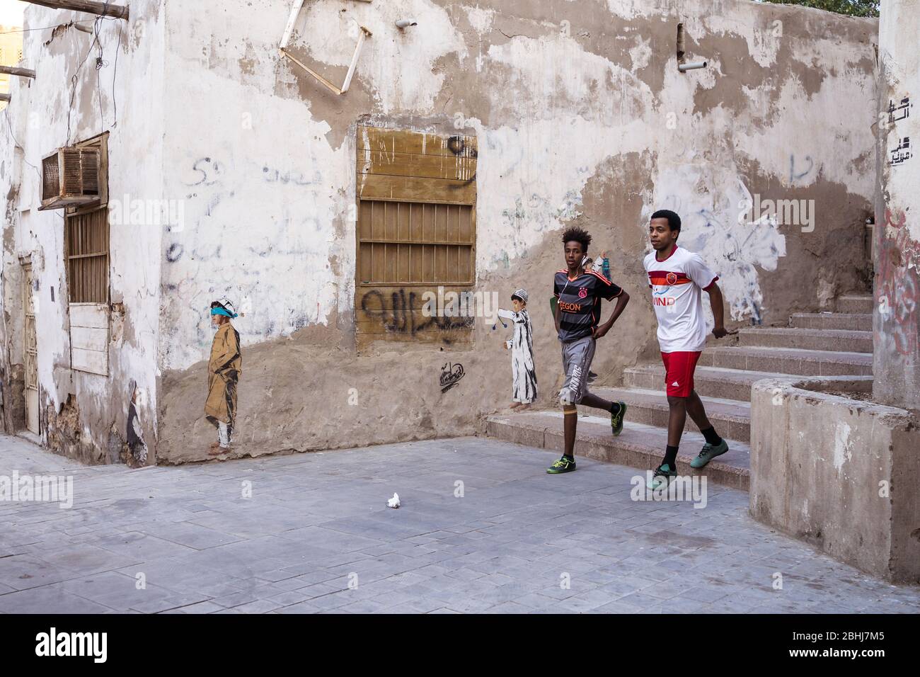 Jeddah / Saudi Arabia - January 16, 2020: two young boys walking in the streets of Jeddah with graffiti in the walls Stock Photo