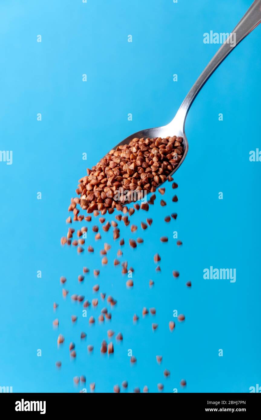Organic Cereal Grains. Raw Buckwheat Seeds Falling from Spoon on Blue