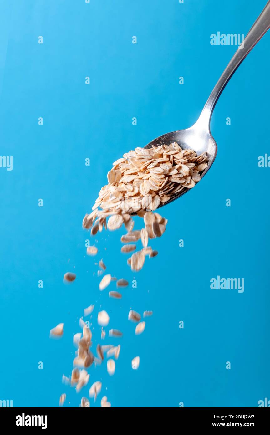 Organic Cereal Grains. Raw Oatmeal Flakes Falling from Spoon on Blue