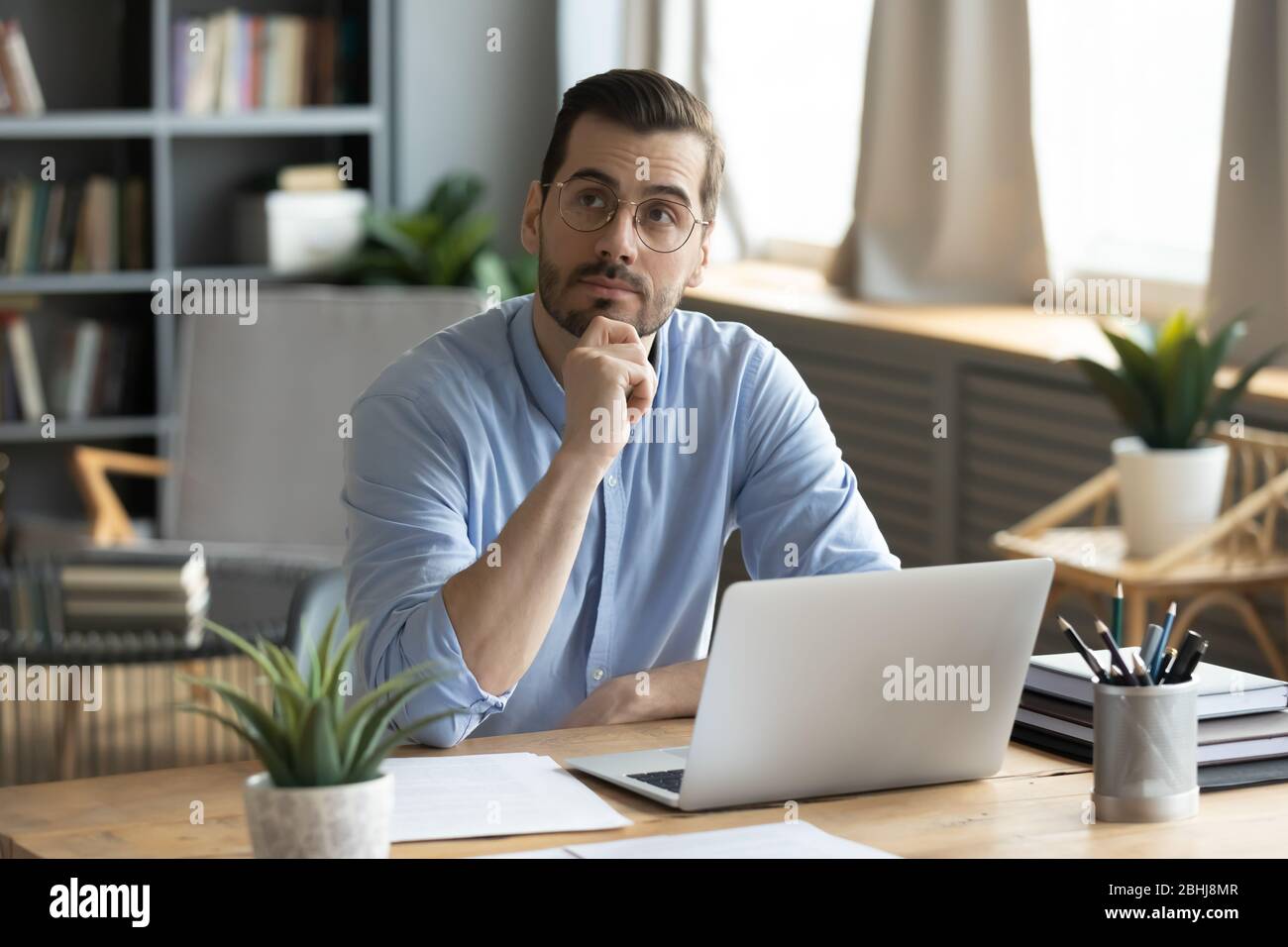 Thoughtful businessman wearing glasses touching chin, pondering ideas Stock Photo