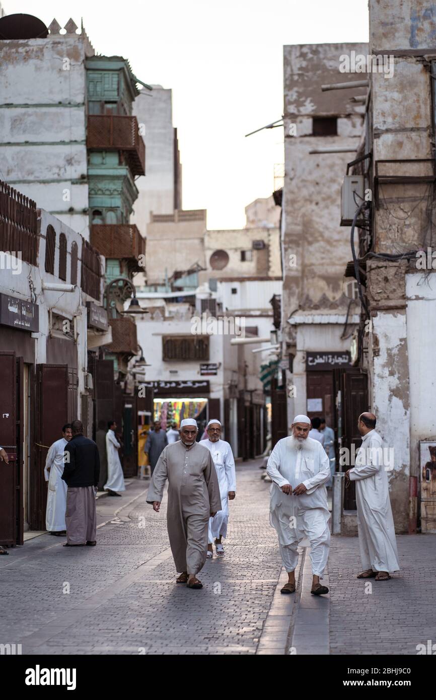 Jeddah / Saudi Arabia - January 16, 2020: Muslim men wearing traditional Muslim clothes walking in frong of historic colorful building in Al-Balad Stock Photo