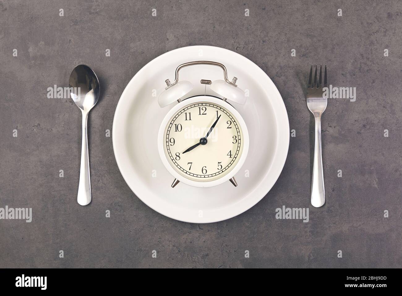 Alarm clock with spoon and fork on plate the table. Time to eat Stock Photo