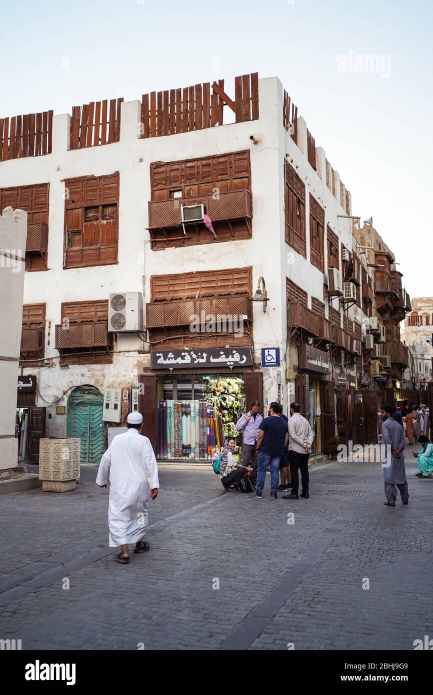 Jeddah / Saudi Arabia - January 16, 2020: Muslim men wearing traditional Muslim clothes walking in front of historic colorful building in Al-Balad Stock Photo