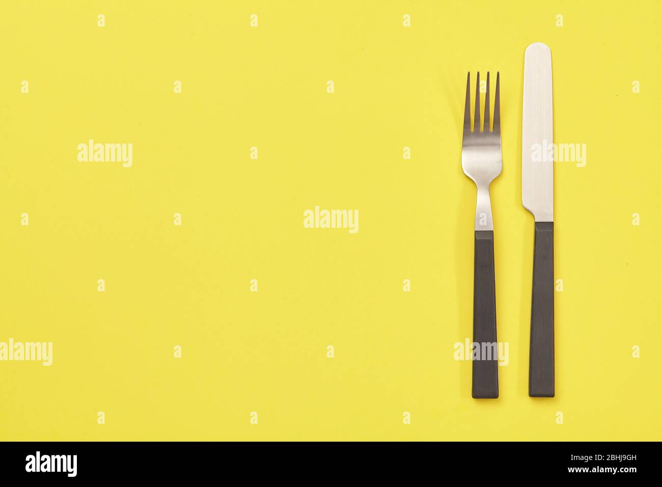 Black knife and fork on yellow background. Top view Stock Photo
