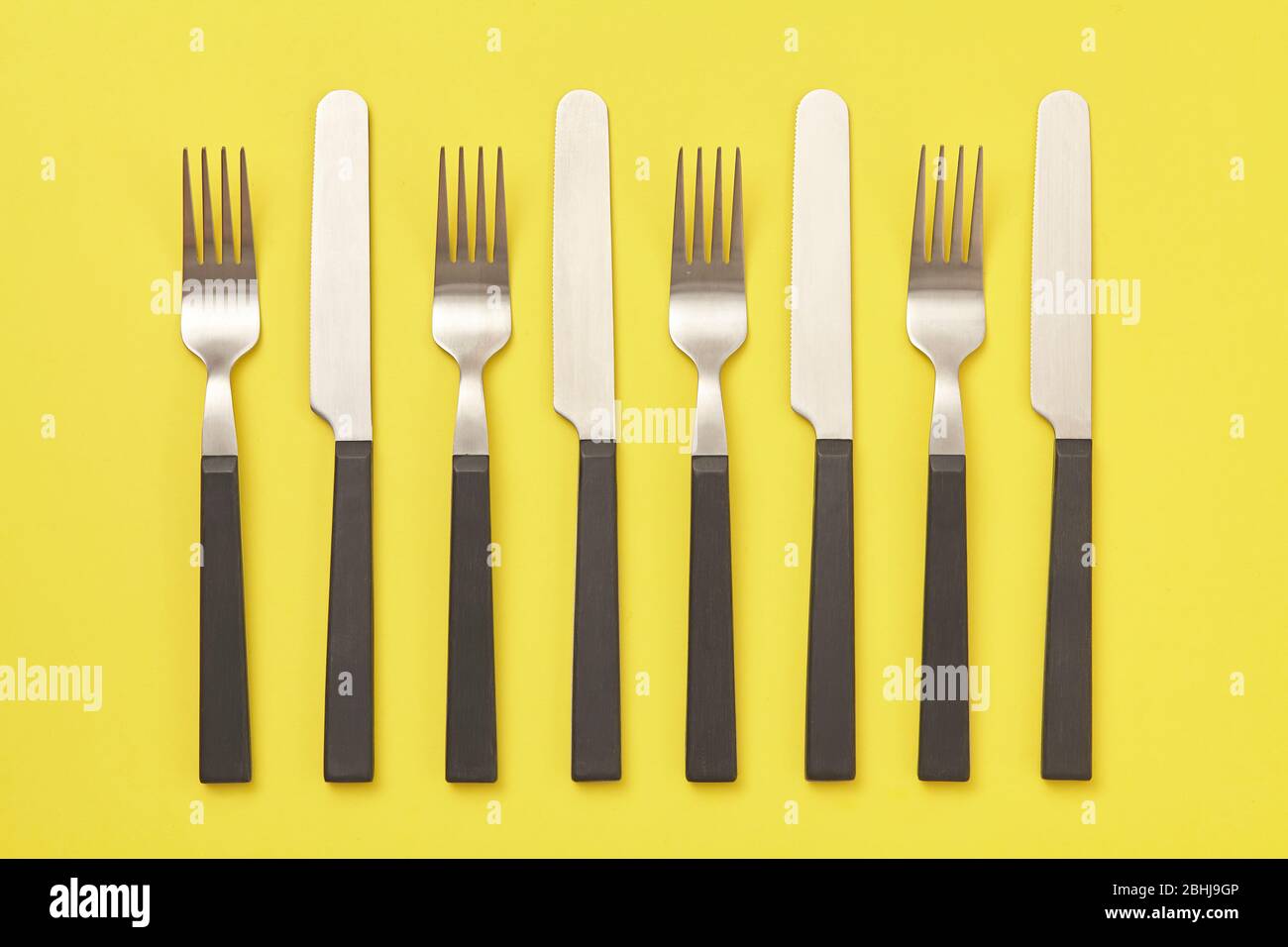 Black knife and fork on yellow background. Top view Stock Photo