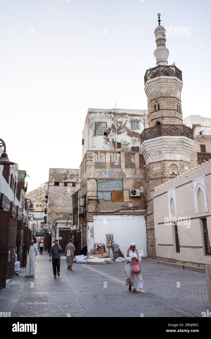 Jeddah / Saudi Arabia - January 16, 2020: Muslim man wearing traditional clothes walking in front of old mosque with minaret in the streets of Al-Balad Stock Photo