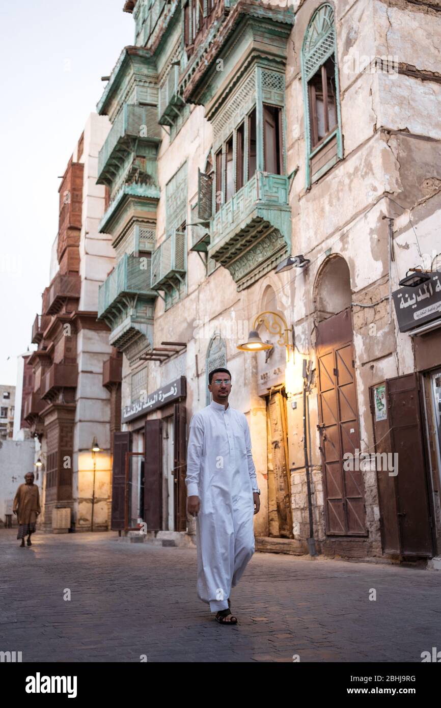 Jeddah / Saudi Arabia - January 16, 2020: Muslim men wearing traditional Muslim clothes walking in front of historic colorful building in Al-Balad Stock Photo