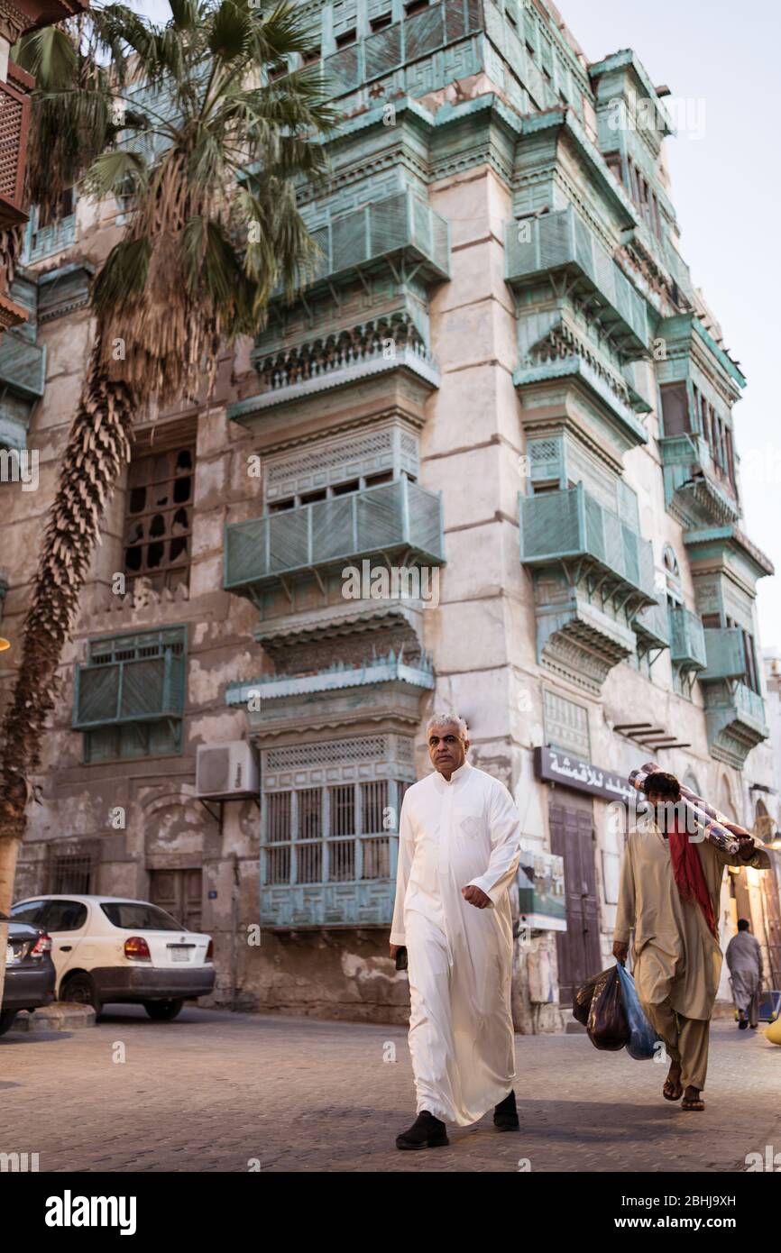 Jeddah / Saudi Arabia - January 16, 2020: Muslim men wearing traditional Muslim clothes walking in front of historic colorful building in Al-Balad Stock Photo