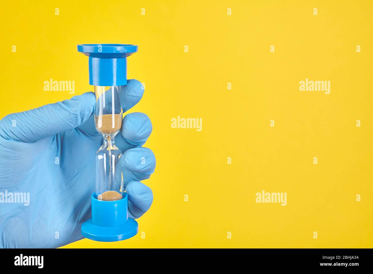 Dentist holding sand glass on yellow background. Copy space Stock Photo