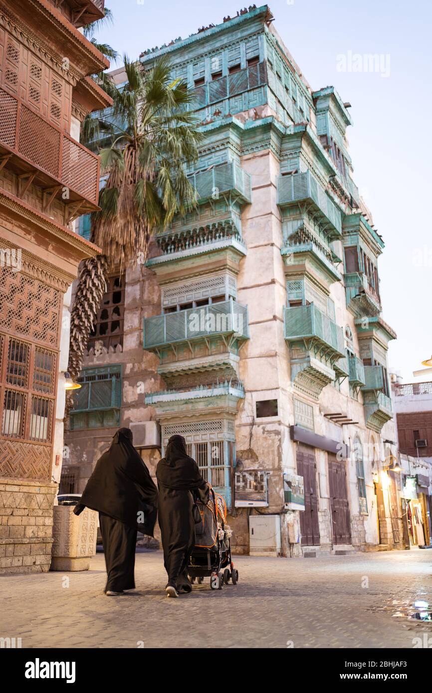 Jeddah / Saudi Arabia - January 16, 2020: Two Muslim women wearing abaya and carrying stroller in historical downtown Al-Balad with colorful building in background Stock Photo