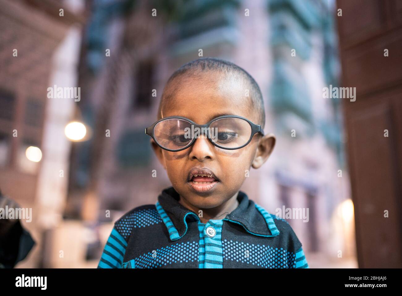 Jeddah / Saudi Arabia - January 16, 2020: Portrait of cute Saudi little boy with glasses with colorful historic buildings of downtown Jeddah in the background Stock Photo