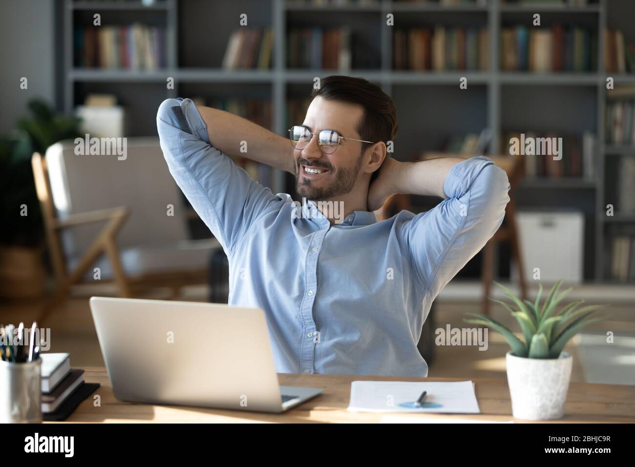 Smiling businessman leaning back in chair, dreaming about future Stock