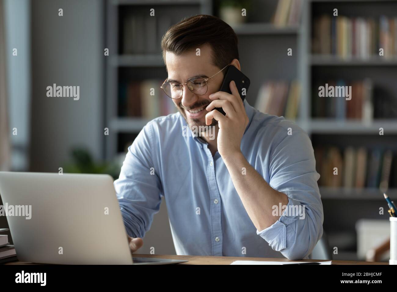 Smiling businessman talking on phone, looking at laptop screen Stock Photo