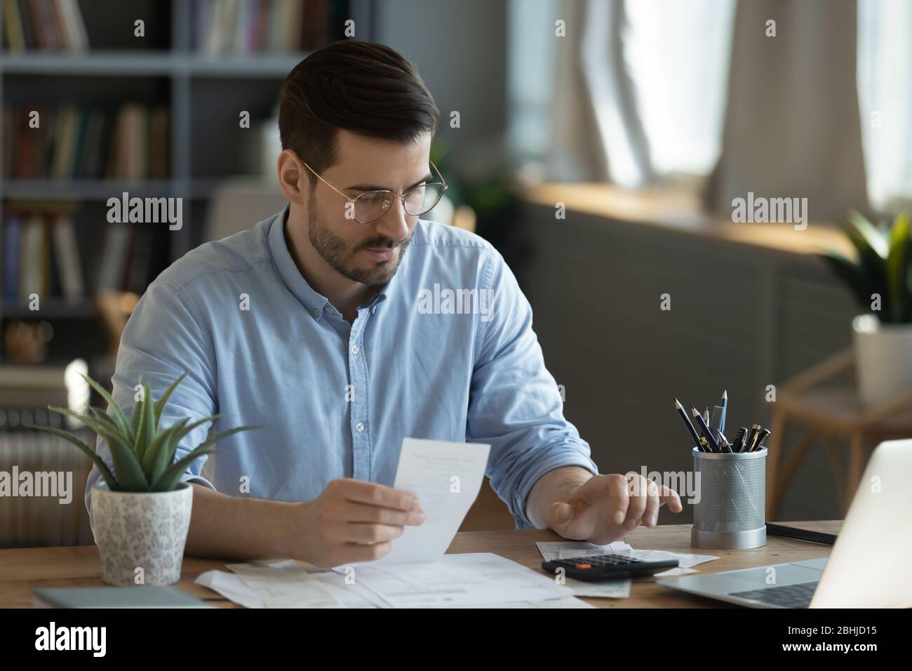 Serious man wearing glasses checking bills, using calculator Stock Photo