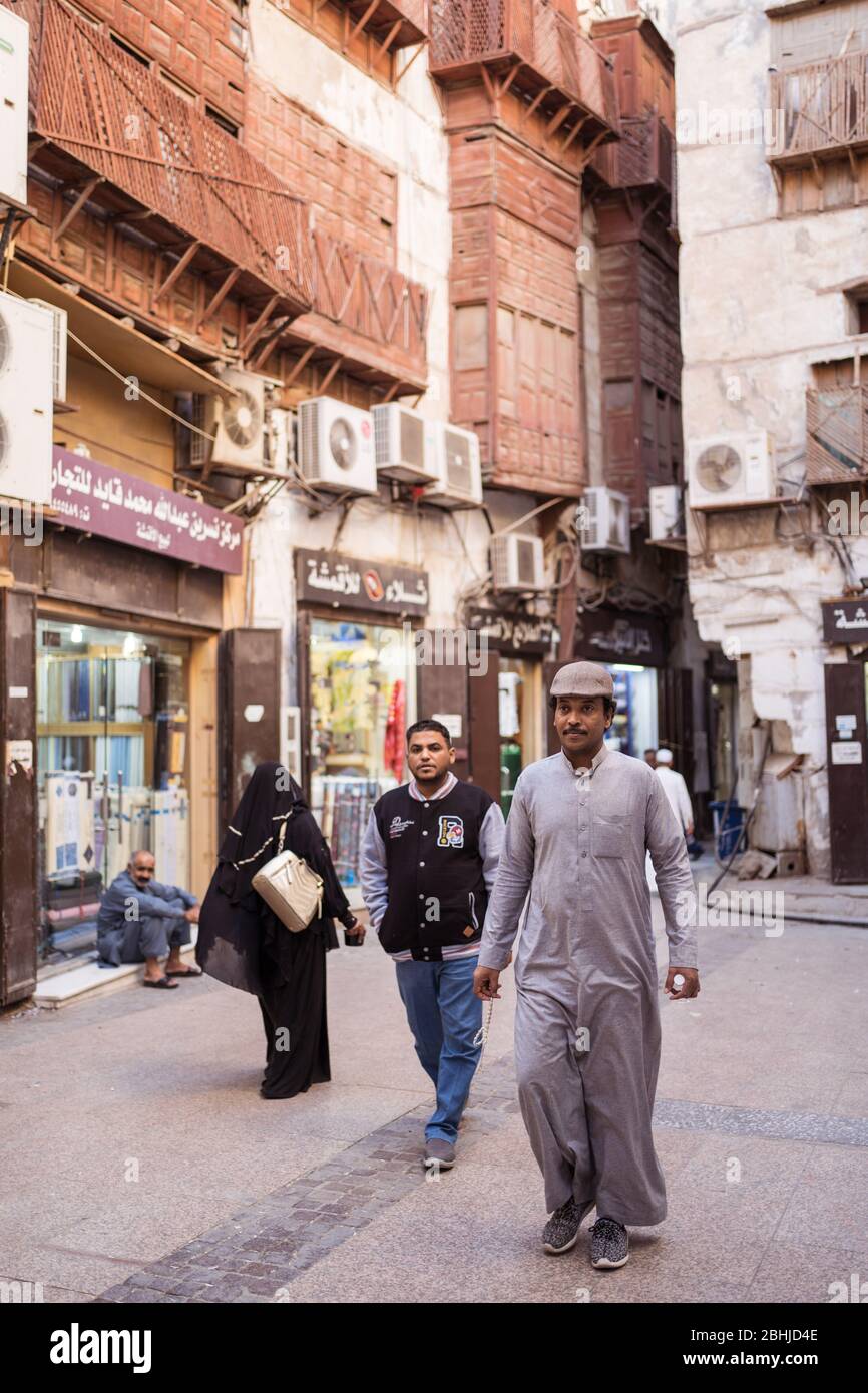 Jeddah / Saudi Arabia - January 16, 2020: Muslim man wearing traditional Muslim clothes walking in front of wooden building in historic Al-Balad Stock Photo